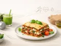 Jak zrobić lasagne? Pyszna, warstwowa lasagne z mięsem mielonym i szpinakiem, obok zielony koktajl, hantle i mata do ćwiczeń.