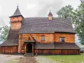 Drewniany kościół w Dębnie, z charakterystyczną wieżą i gontowym dachem, otoczony zielenią.