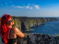 Kobieta z rudymi włosami podziwia majestatyczne klify Moheru. Słońce odbija się w jej okularach, a ocean lśni w oddali.