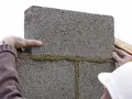 Pose de parpaings avec mortier. On voit les mains d'un maçon ajustant une brique. La question est : combien de mortier pour 1m2 de parpaing ?