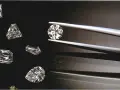 Diverse pietre preziose, tra cui diamanti, brillano su sfondo scuro. Una pinzetta tiene un diamante rotondo, mentre altri, di varie forme, sono disposti intorno.