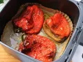 Tres pimientos rojos asados en freidora de aire, con la piel arrugada y jugosos, listos para disfrutar.