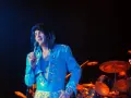 Elvis Presley, in einem glitzernden blauen Anzug, singt ins Mikrofon. Ein Bild, das an seine legendären Elvis Presley Filme erinnert.