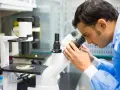 Mężczyzna w niebieskiej fartuchu laboratoryjnym bada próbkę pod mikroskopem, kluczowy element w diagnostyce patomorfologia.