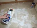 Main tenant tente de nettoyer un voile de ciment qui ne part pas sur le carrelage avec un produit.