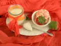 Yogur cremoso en frasco con fresas y trozos de yogur en un plato blanco sobre tela naranja.
