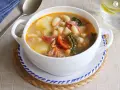 Un tazón blanco de caldo gallego con patatas, alubias, chorizo y grelos.