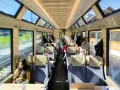 Passengers enjoy the scenic views from the panoramic windows of a train on the Golden Pass Line, with mountains visible outside.