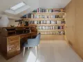 Scrivania in legno massiccio e libreria moderna illuminata, un perfetto esempio di come abbinare e mischiare arredamento classico e moderno in uno studio mansardato.