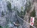 Un emozionante ponte tibetano in Piemonte attraversa una gola rocciosa, con un torrente sottostante e pini aggrappati alle pareti.