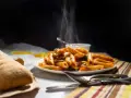 Piatto fumante di penne alla vodka, con pane croccante e posate. Un classico confortante.