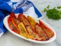 Peperoni gratinati al forno, rossi e gialli, cotti alla perfezione con pangrattato e erbe aromatiche, serviti su un piatto bianco con un tovagliolo blu.