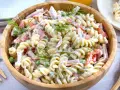 Ein großer Holzteller voller cremigen Nudelsalat mit Schinken, Erbsen und Paprika. Mit Dill garniert, sieht er aus wie der beste Nudelsalat!