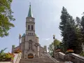 Słynny kościół w Zakopanem, z kamienną fasadą i zieloną wieżą, otoczony drzewami i ozdobiony czerwonymi kwiatami.