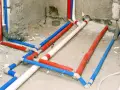 Skomplikowana instalacja wodna z rurami w kolorach czerwonym, niebieskim i białym, przygotowana do ukrycia pod tynkiem.