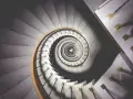 Kręcone schody z marmuru i drewna, tworzące spiralę przypominającą ciąg Fibonacciego w architekturze.