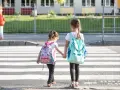 Dwie dziewczynki z plecakami idą za rękę przez pasy. Od ilu lat dziecko może samo chodzić po mieście?