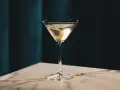 Elegancki gin z wermutem, ozdobiony skórką cytryny, czeka na stole z marmurowym blatem.