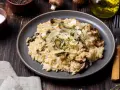 Kremowe risotto z pieczarkami, posypane parmezanem i ziołami, na ciemnym talerzu.
