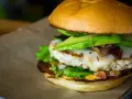 Pyszny hamburger z kurczakiem, awokado, serem i bekonem na brązowym papierze.