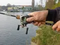 Hand hält Angelrute mit Baitcast-Rolle, die grüne baitcast schnur ist gut sichtbar.
