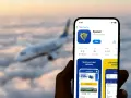 Ręka trzyma smartfon z aplikacją Ryanair, gotową do rezerwacji lotu. W tle widać samolot lecący wśród chmur.
