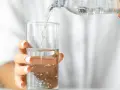 Eine Hand hält ein Glas, in das kohlensäurehaltiges Mineralwasser gegossen wird.