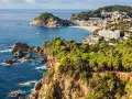 Scenic view of the Costa Brava coastline, a perfect stop on the way to Barcelona, with rugged cliffs, pine forests, and a charming town nestled by the sea.