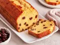 Ein saftiger Rosinenkuchen mit goldbrauner Kruste, auf einem weißen Teller angerichtet. Rosinen sind gut sichtbar im Teig verteilt.