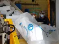 Pracownik w masce i przyłbicy przygotowuje styropian do recyklingu. Duży worek z logo Knauf Circular symbolizuje proces recyklingu styropianu.