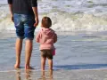 Ojciec i dziecko na plaży, cieszący się wspólnym urlopem ojcowskim 9 tygodni.