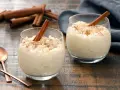 Dos copas de cremoso arroz con leche, espolvoreado con canela y decorado con una rama de canela.