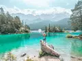 Frau mit ausgebreiteten Armen und Hut am türkisfarbenen Eibsee in Bayern, im Hintergrund Berge und Wald.