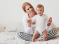 Uśmiechnięta mama pomaga swojemu 8 miesięcznemu dziecku w pierwszych krokach na łóżku.