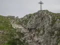 Grupa turystów wspina się po skalistym zboczu w kierunku krzyża na szczycie. Trudno określić, ile idzie się na Giewont, ale widok jest imponujący.