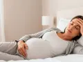 Zmęczona ciężarna leży w łóżku, dotykając czoła. Senność w ciąży to częsty objaw.