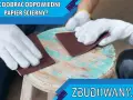 Ręce w białych rękawiczkach szlifują drewniany stołek papierem ściernym. Dowiedz się, jaki papier ścierny do drewna przed malowaniem będzie najlepszy.