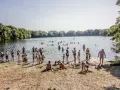 Menschen genießen einen sonnigen Tag im Strandbad Hamburg. Kinder spielen im Sand, während Erwachsene im Wasser planschen.