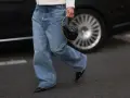 Dziewczyna w szerokich jeansach i białej marynarce trzyma okrągłą, czarną, pikowaną torebkę na złotym łańcuszku.
