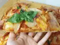 Una fetta di pizza di patate dorata, guarnita con basilico fresco, pronta per essere gustata.