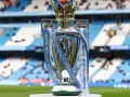 Trofeum za mistrzostwo Anglii, błyszczące i ozdobione wstążkami Premier League, stoi na tle stadionu.