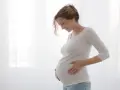 Uśmiechnięta ciężarna kobieta dotyka brzucha. Myśli o przyszłości i zasiłku macierzyńskim.