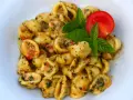 Pyszne makaron orecchiette z sosem pomidorowo-ziołowym, udekorowane listkami bazylii i pomidorem.