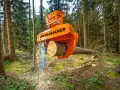 Pomarańczowe maszyny leśne do zrywki drewna, model Woodcracker, tną pień drzewa w lesie.