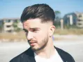 Joven con barba y cortes de pelo hombre elegante, peinado hacia atrás con degradado.
