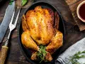 Pollo al horno dorado y jugoso, servido en sartén de hierro fundido con romero. Acompañado de salsa barbacoa y cubiertos rústicos.