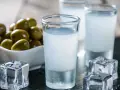 Raki, ein Getränk, das oft mit Griechenland assoziiert wird, wird aus Trauben hergestellt. Hier sind Gläser mit Raki, Eiswürfel und Oliven.