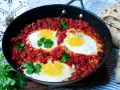 Herzhaftes Shakshuka-Rezept in einer Pfanne mit pochierten Eiern in würziger Tomatensoße, garniert mit Koriander. Dazu gibt es Fladenbrot.