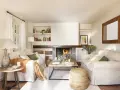 Salón acogedor con chimenea encendida, sofás blancos, mesa de centro de madera y detalles decorativos.