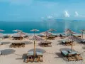 Plaża z leżakami i parasolami, idealna na relaks nad morzem. W oddali widać góry i błękitne niebo.